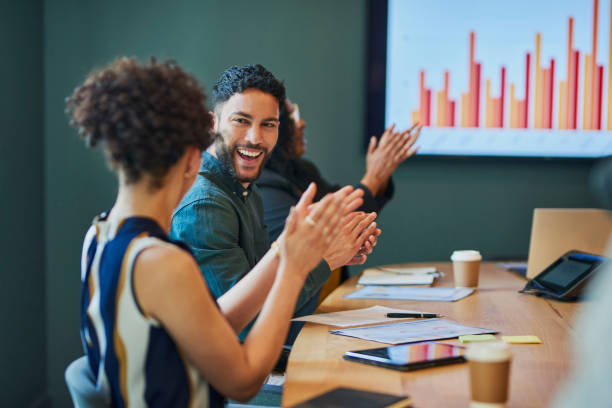 A team in a meeting clapping and smiling, with a chart showing positive results in the background.