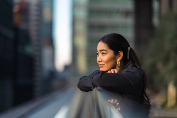 A woman looking thoughtfully into the distance with a blurred city background.