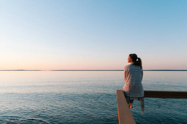 Person sitting peacefully on dock by water at sunset