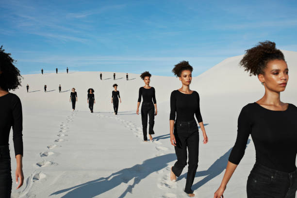 Line of people in black clothing walking across white sand dunes, representing unified brand scaling across different local markets